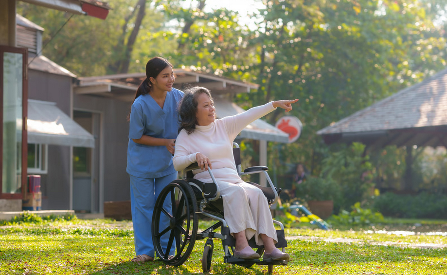 A female hospice nurse in blue scrubs assisting a senior woman in a wheelchair outside, demonstrating comfort care at home for patients with advanced heart failure.