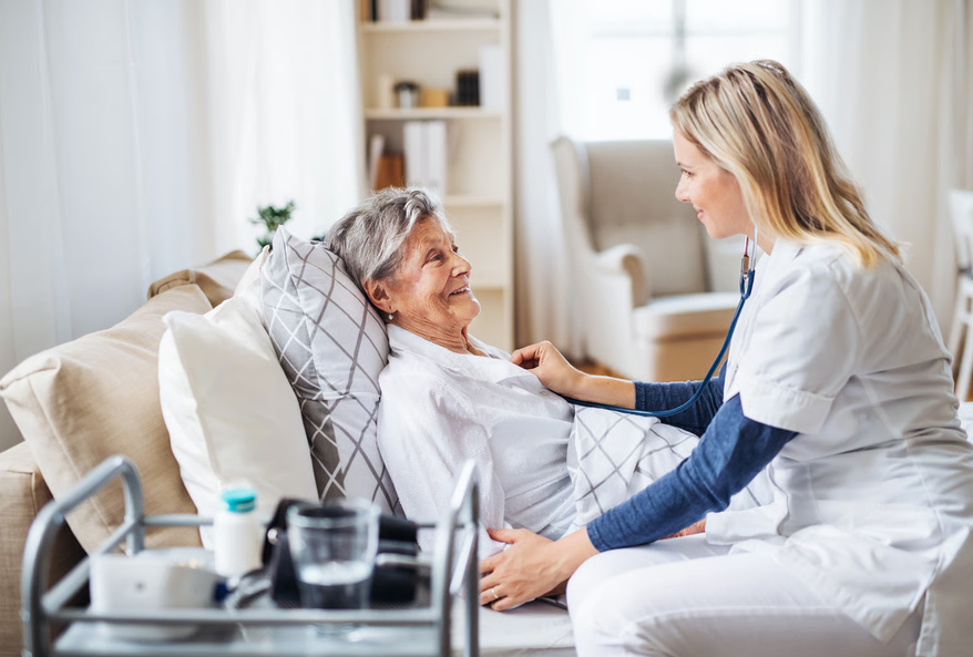 A compassionate hospice nurse using a stethoscope to check a senior woman resting comfortably in bed.