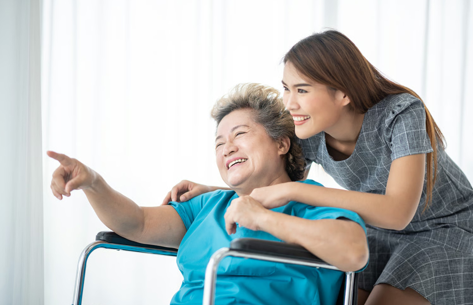A smiling senior woman sitting in a wheelchair with a supportive female caregiver standing beside her in an Alpharetta hospice care setting.